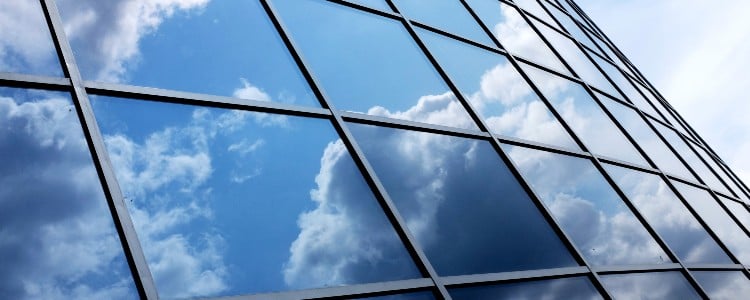 Reflection of clouds on a modern glass building, showcasing a blue sky with white and gray clouds in geometric window panels.