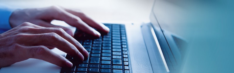 Close-up of hands typing on a laptop keyboard, with a soft-focus background, conveying a sense of focused work or technology use.
